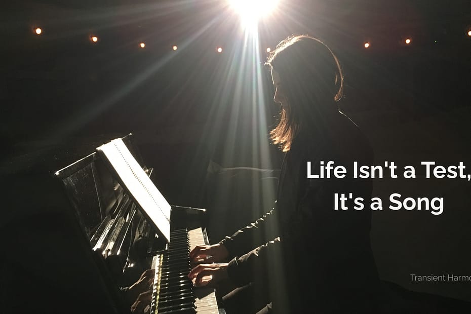 A pianist plays alone on a darkened stage under dramatic overhead light — Life Isn't a Test, It's a Song, a reflective essay by Braddon Damien White, Transient Harmony